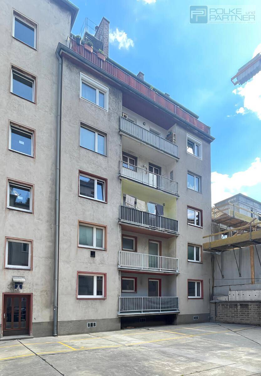 Seitenansicht des Mehrfamilienhauses mit Balkonen und einer gepflegten Fassade unter blauem Himmel.