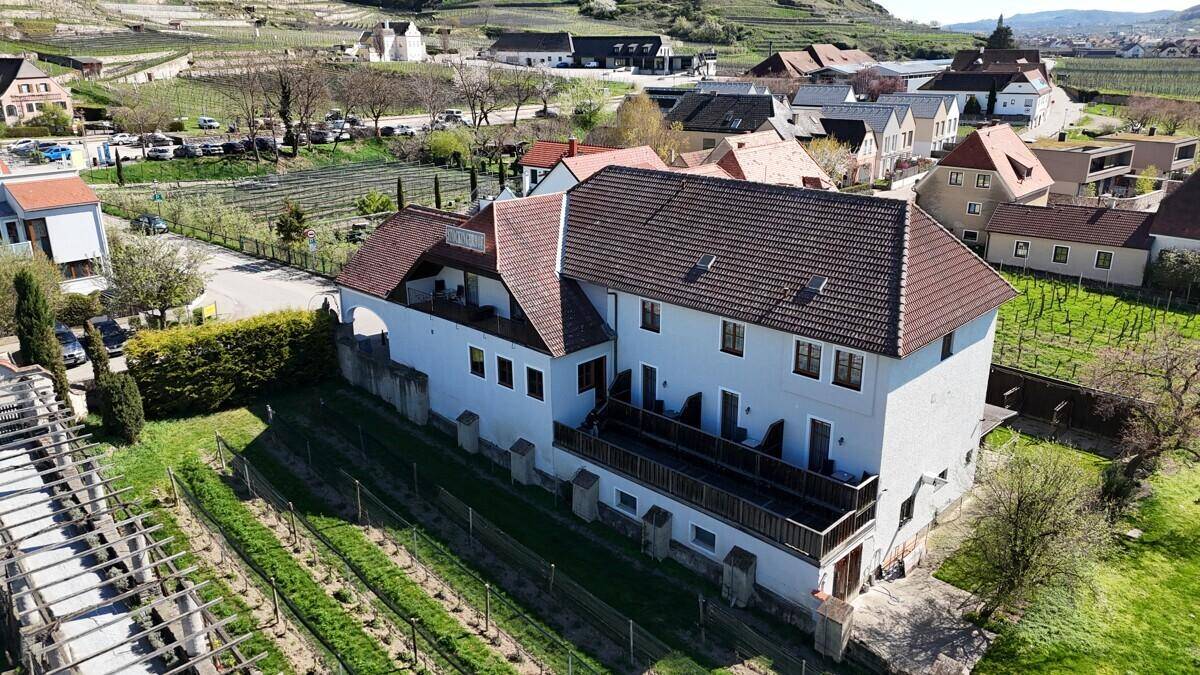 Luftaufnahme eines Gebäudes mit mehreren Terrassen und einem Garten, umgeben von Weinbergen und anderen Häusern.