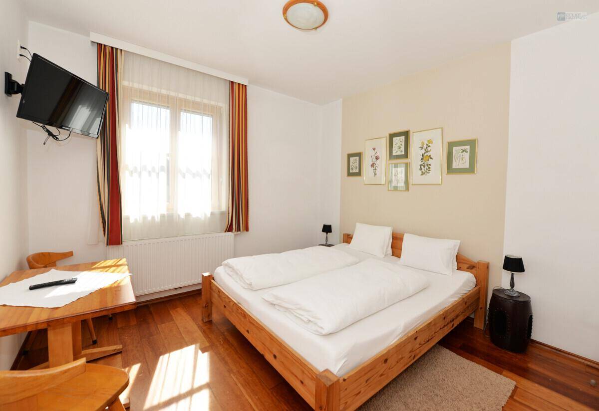 Komfortables Schlafzimmer mit Doppelbett, Holzfußboden und einem kleinen Essbereich mit Fernseher.