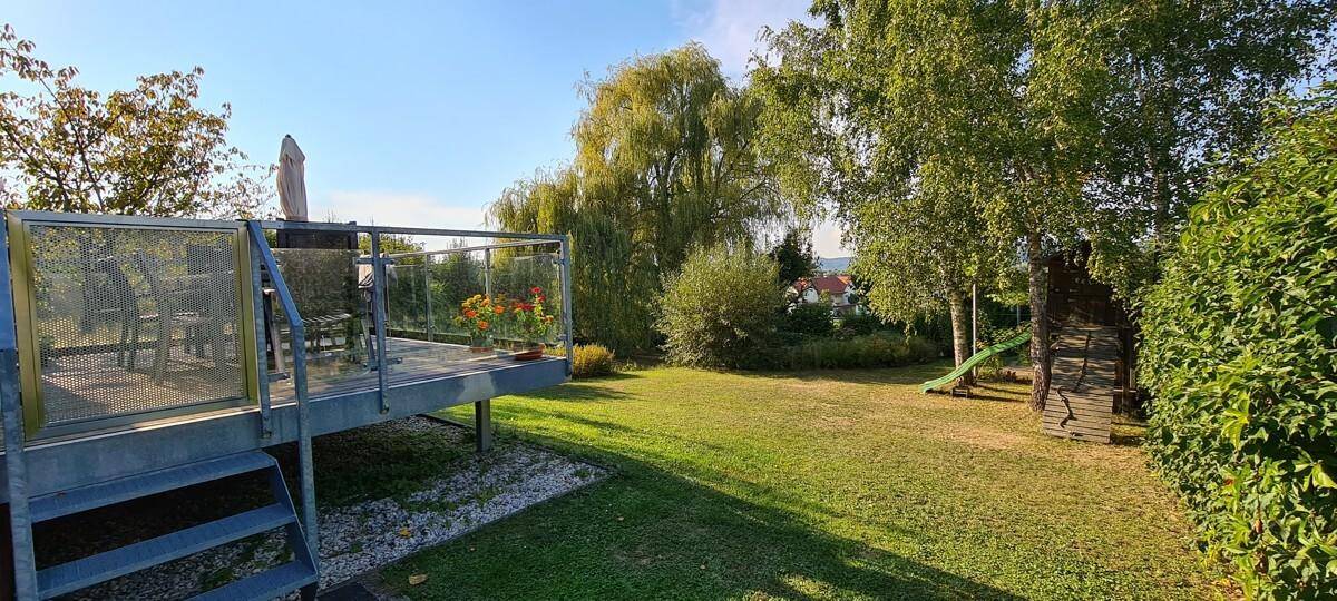Erhöhte Terrasse mit Glasgeländer und Blick auf den Garten mit Spielgeräten.
