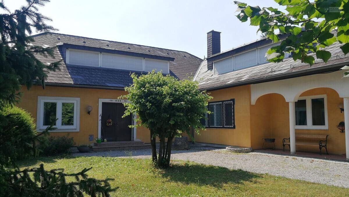 Ansicht des gelben Hauses mit Eingangsbereich, Schornstein und grüner Umgebung.