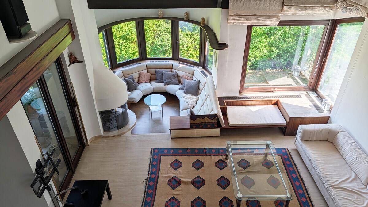 Geräumiges Wohnzimmer von oben gesehen mit Kamin, großen Fenstern und gemütlicher Sitzecke.