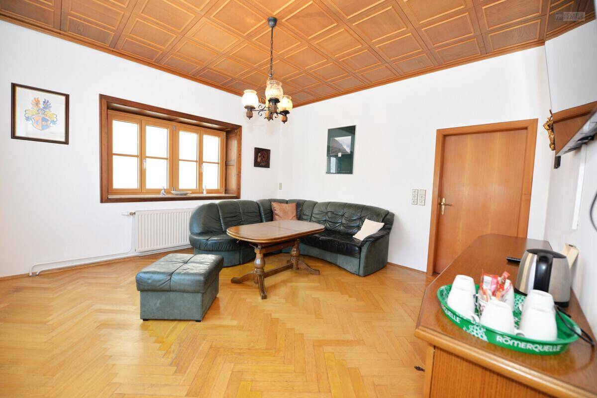 Gemütliches Wohnzimmer mit Ledersofa, Fischgrätparkett und einer Holzdecke mit Kassettenmuster.