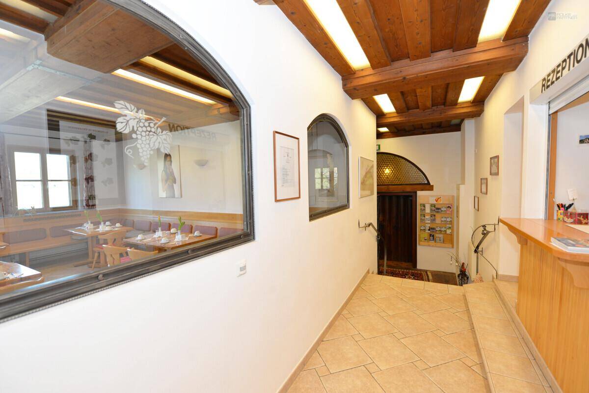 Heller Flur mit Rezeption, Fliesenboden und Blick durch eine Glasscheibe in einen Speisesaal.
