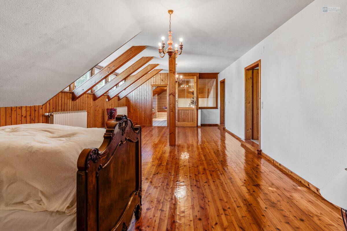 Geräumiges Schlafzimmer im Dachgeschoss mit glänzendem Holzboden und Holzbalken.