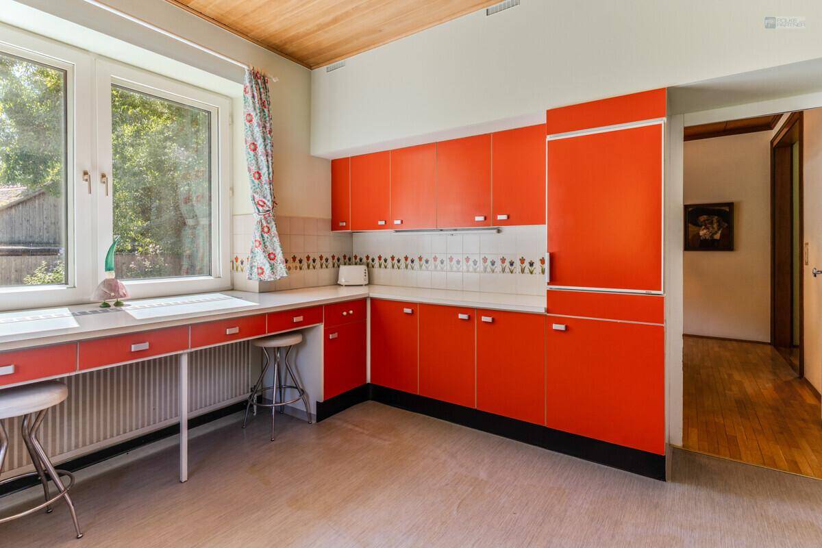 Küche im Retro-Stil mit leuchtend orangefarbenen Schränken und großem Fenster.