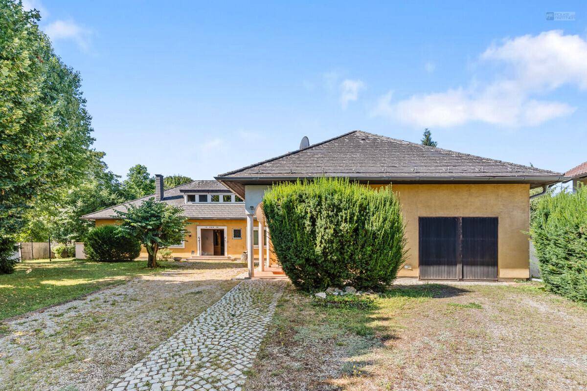 Vorderansicht des Hauses mit Kiesauffahrt, Garage und gepflegten Büschen.