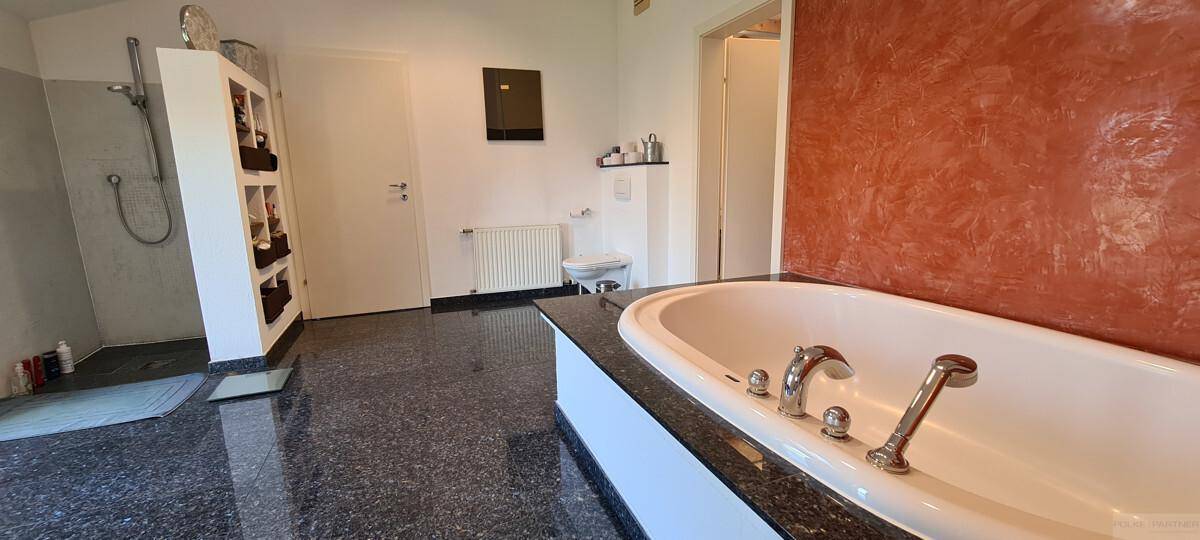Großes Badezimmer mit Badewanne, separater Dusche und dunklem Granitboden.