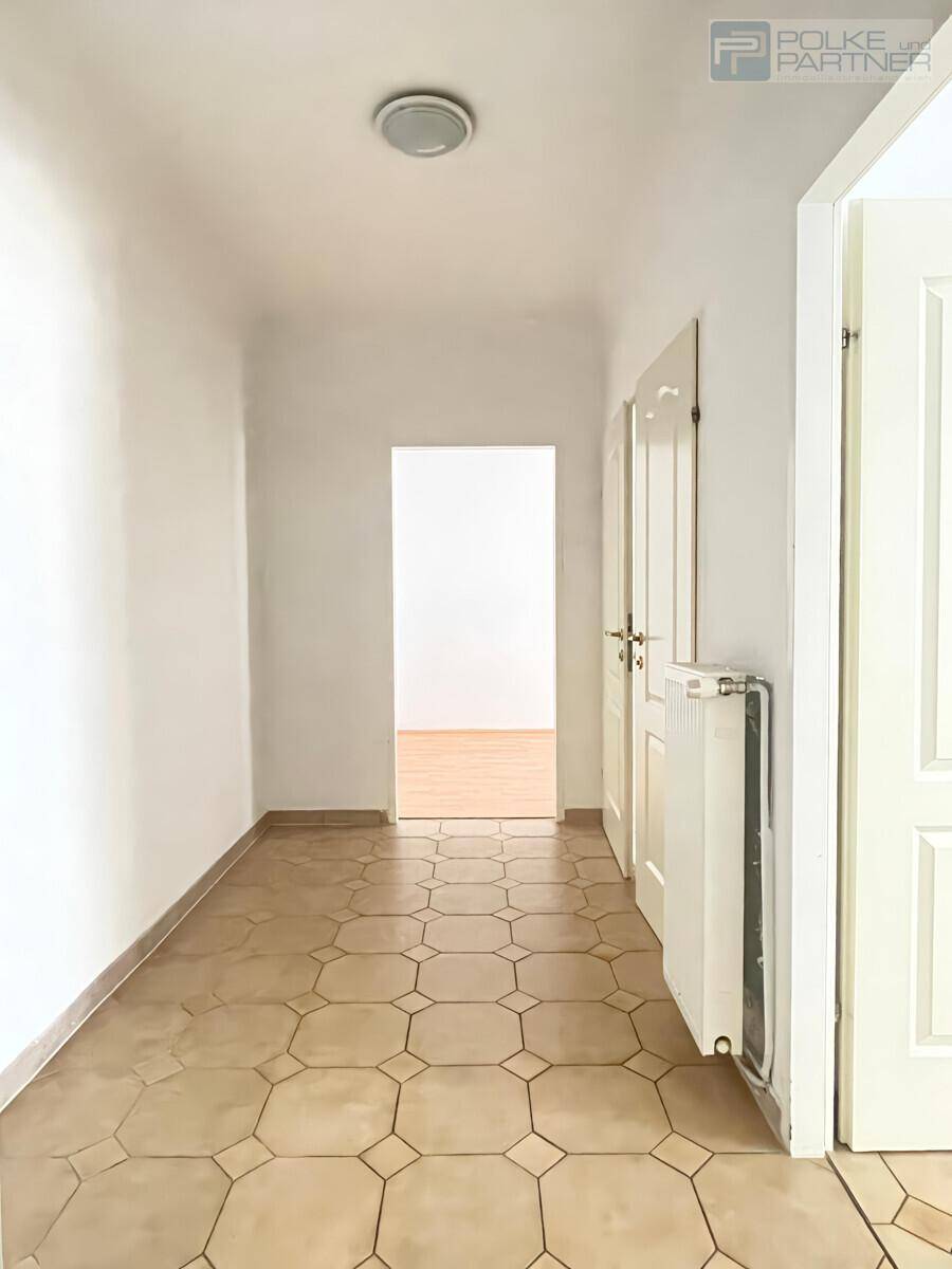 Heller Flur mit Fliesenboden und weißen Wänden, der zu den verschiedenen Zimmern der Wohnung führt.