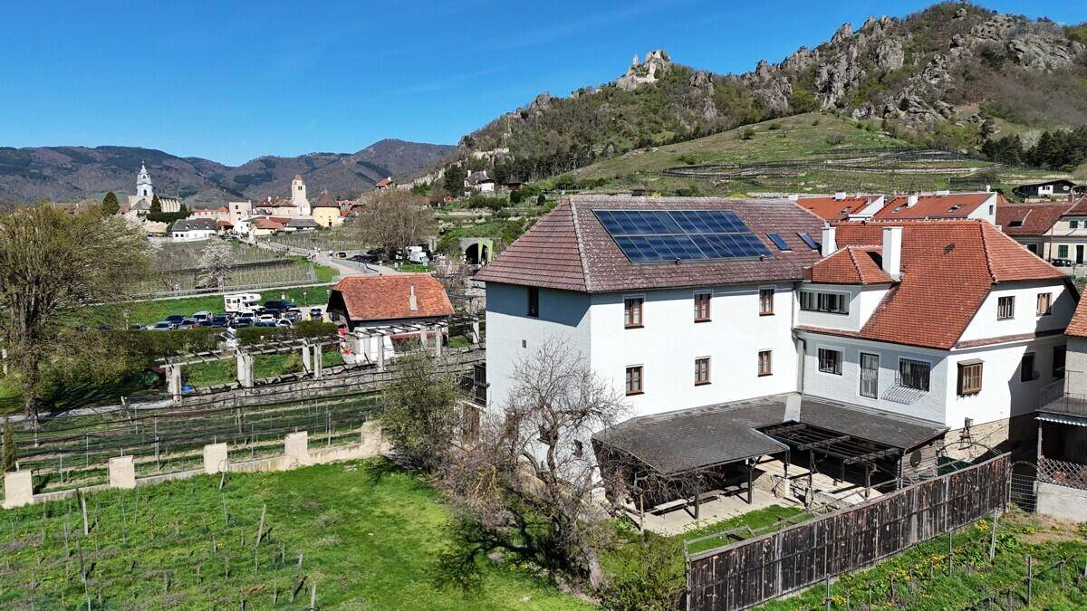 Luftaufnahme eines Gebäudes mit Solaranlage auf dem Dach, umgeben von Weinbergen und einem malerischen Dorf.