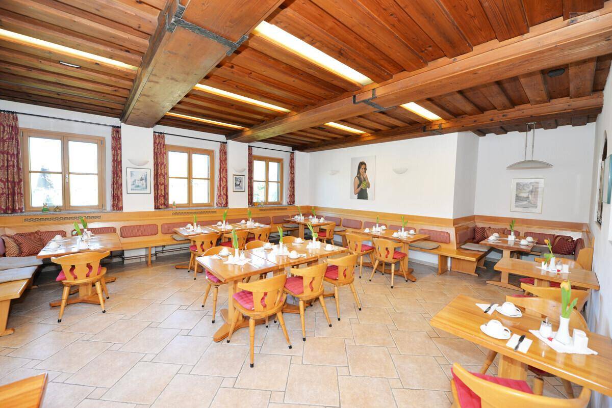 Gemütlicher Speisesaal mit Holztischen, Bänken, Fliesenboden und sichtbaren Holzdeckenbalken.