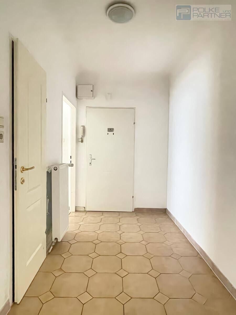 Eingangsbereich mit Fliesenboden und weiß gestrichenen Wänden, inklusive Gegensprechanlage.