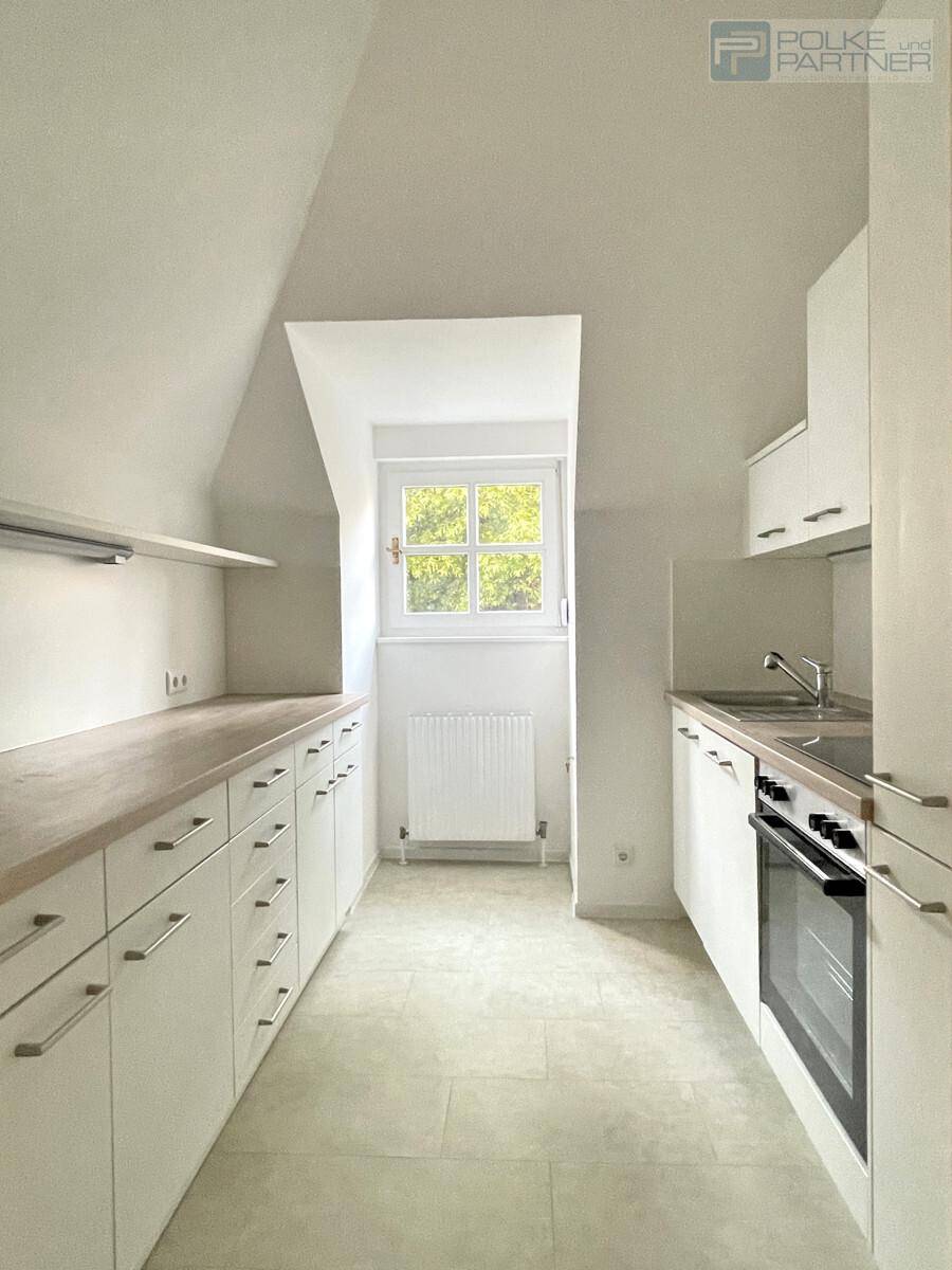 Helle Küche mit weißen Schränken, Holz-Arbeitsplatte, Backofen und Fenster unter Dachschräge.