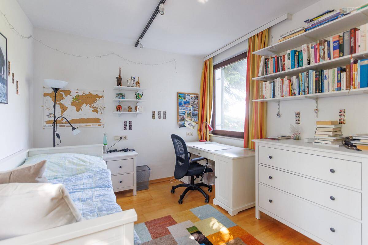 Helles Kinderzimmer mit Schreibtisch, Bücherregalen und farbenfrohem Teppich.