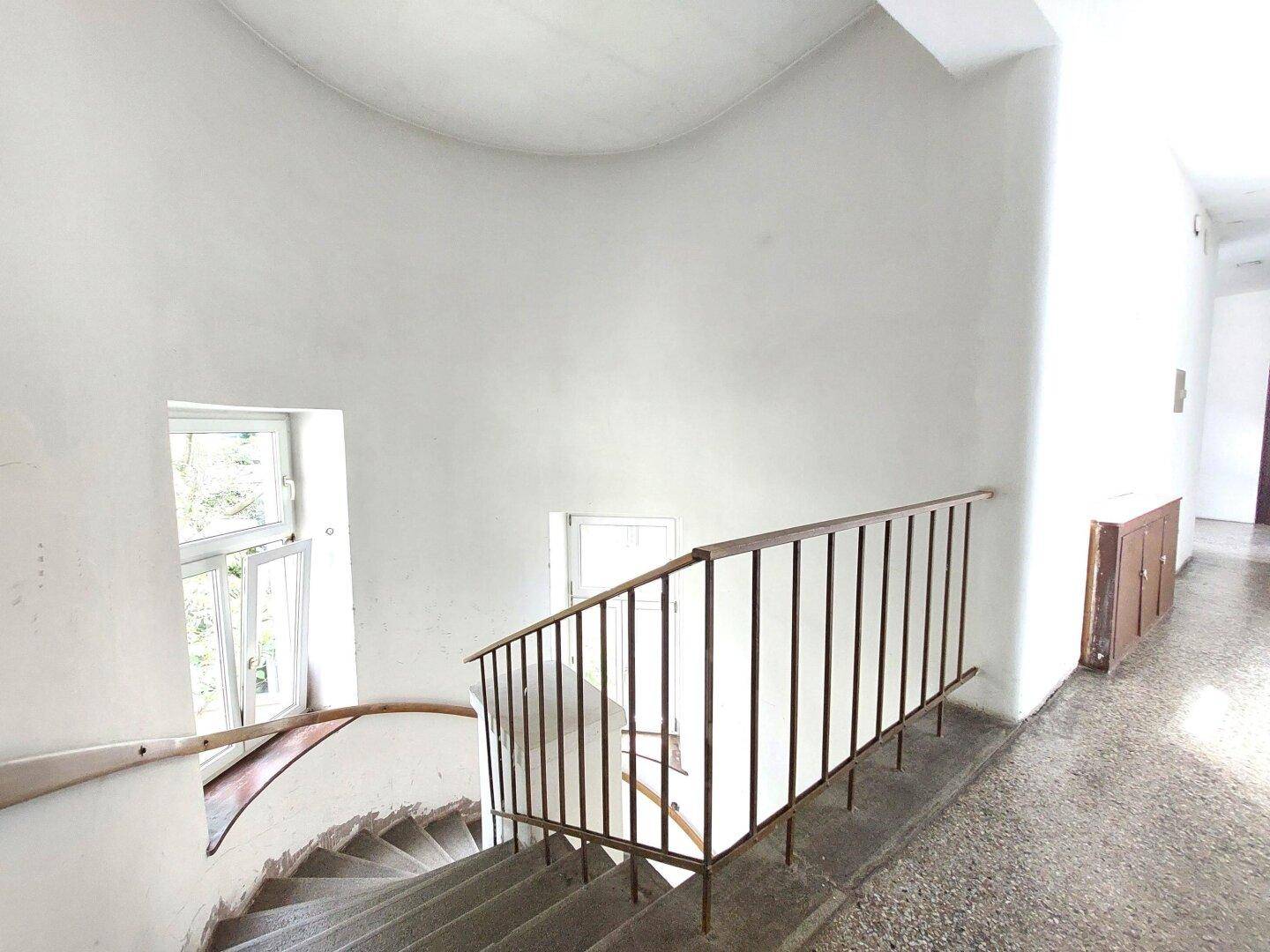 Treppenhaus mit geschwungener Treppe, Geländer und Fenstern für natürliches Licht.