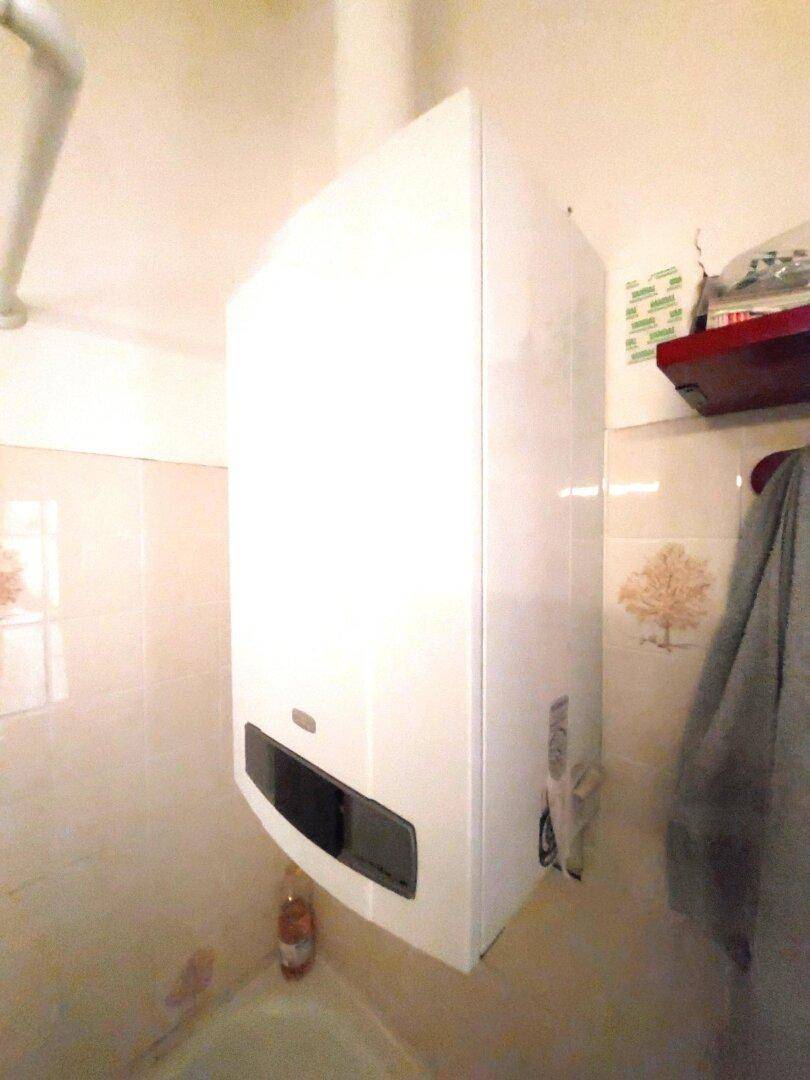 Detailaufnahme eines Warmwasserboilers im Badezimmer mit hellen Fliesen.