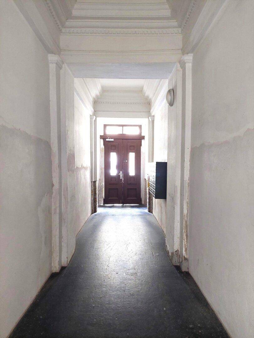 Langer Flur im Eingangsbereich eines Altbaus mit hoher Decke und Doppeltür.
