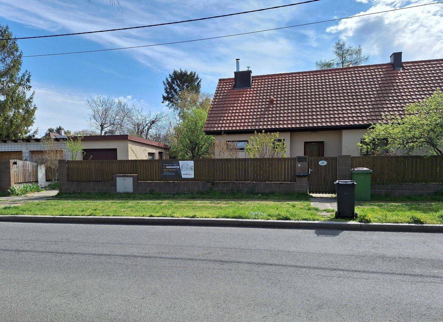 Einfamilienhaus mit rotem Ziegeldach und Holzzaun, von der Straße aus gesehen.