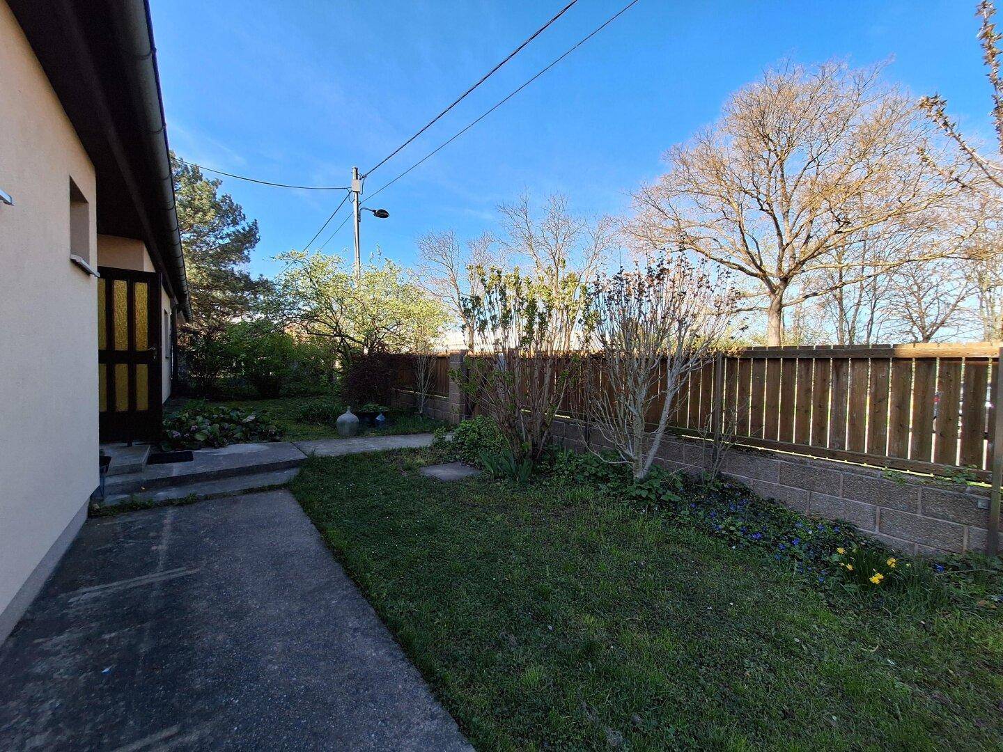 Seitenbereich des Hauses mit einem gepflasterten Weg und einem kleinen Gartenbeet.