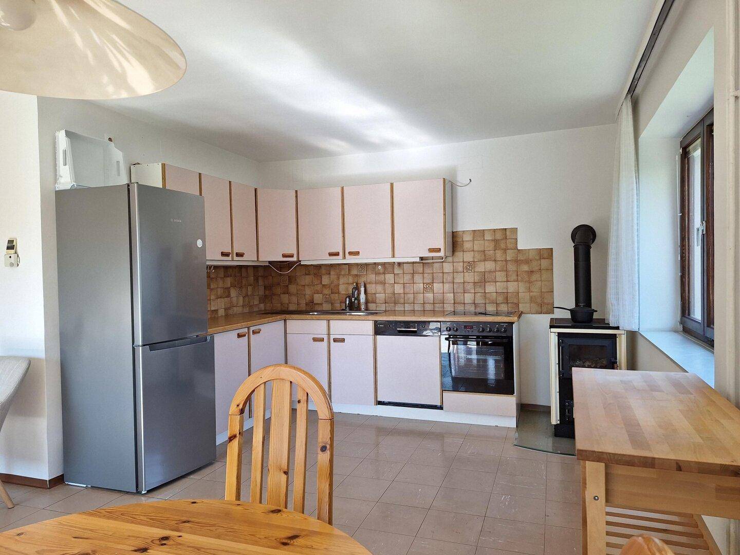 Funktionale Küche mit hellen Schränken, Fliesenboden, Holzofen und Essbereich.