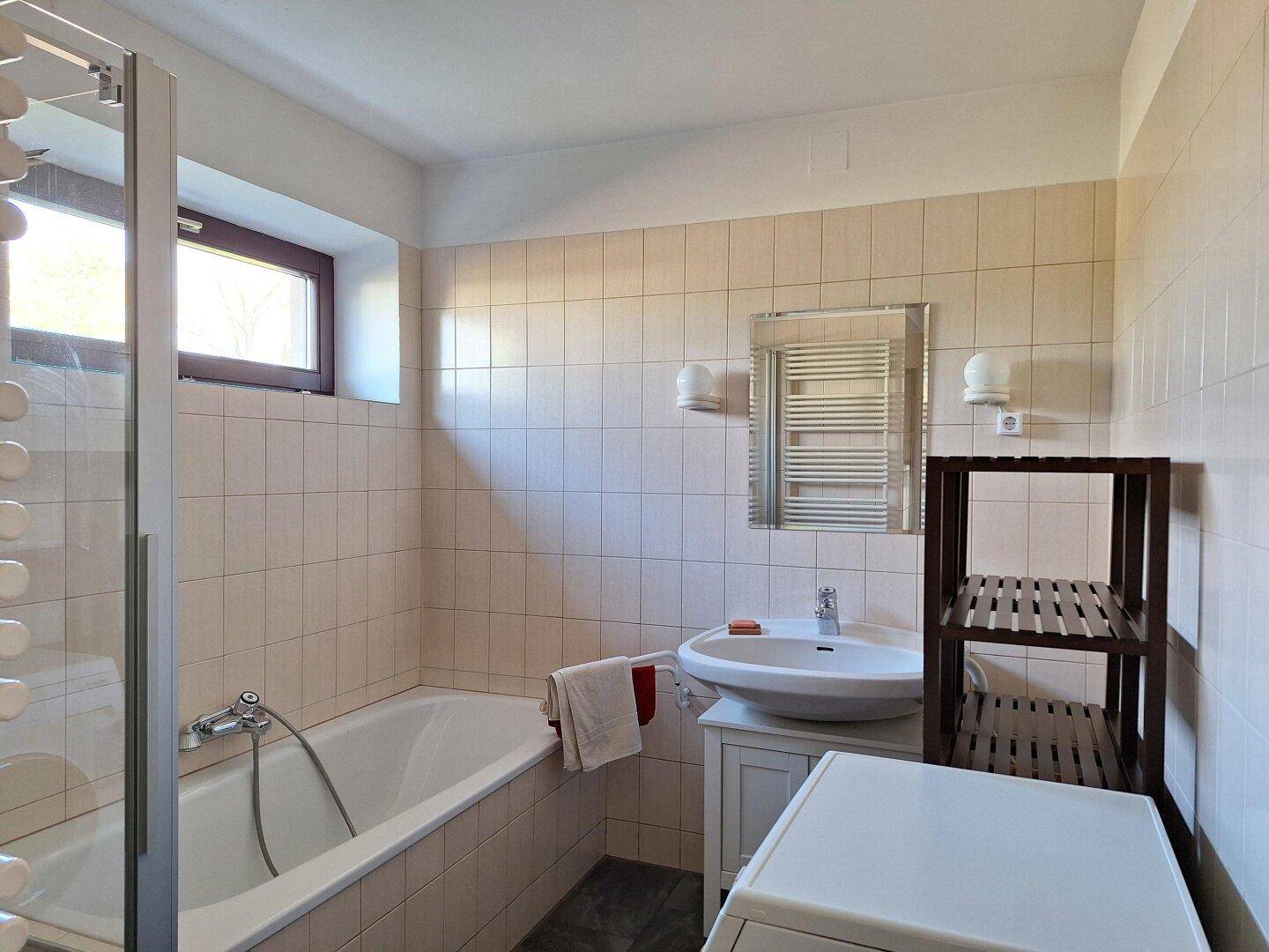 Badezimmer mit Badewanne, Dusche, Waschbecken, Fenster und Handtuchheizkörper.