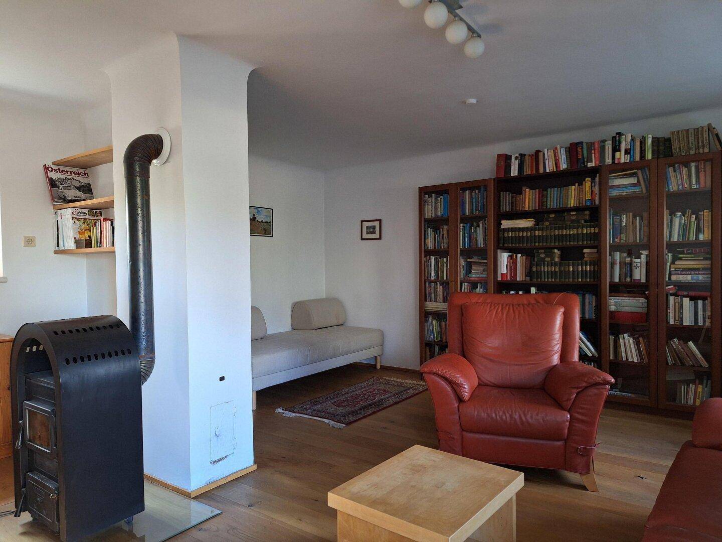 Wohnzimmer mit Holzboden, Kaminofen, bequemen Sitzmöbeln und einer Bücherwand.