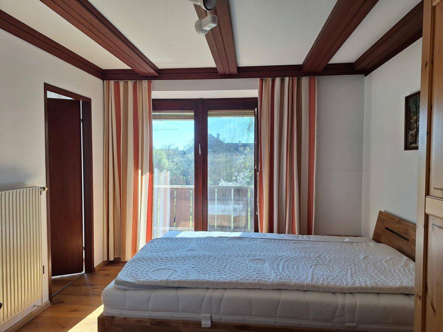 Schlafzimmer mit Holzbalkendecke, Holzboden und direktem Zugang zum Balkon.