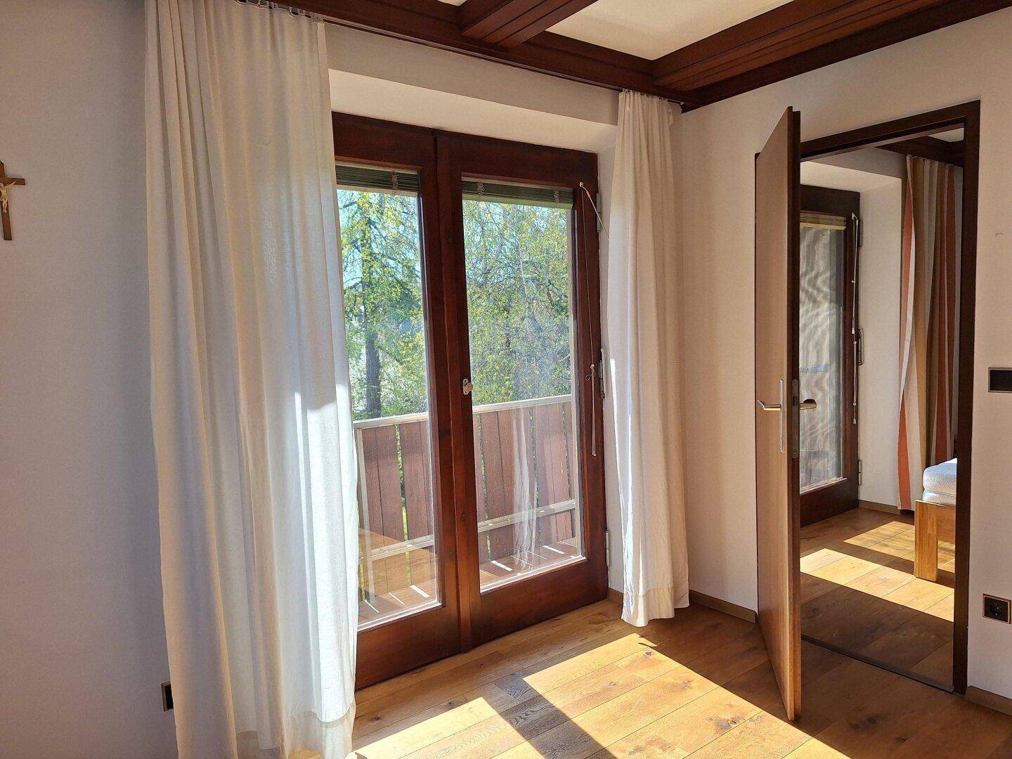 Schlafzimmer mit Holzboden, weißen Vorhängen und Zugang zu einem Balkon.