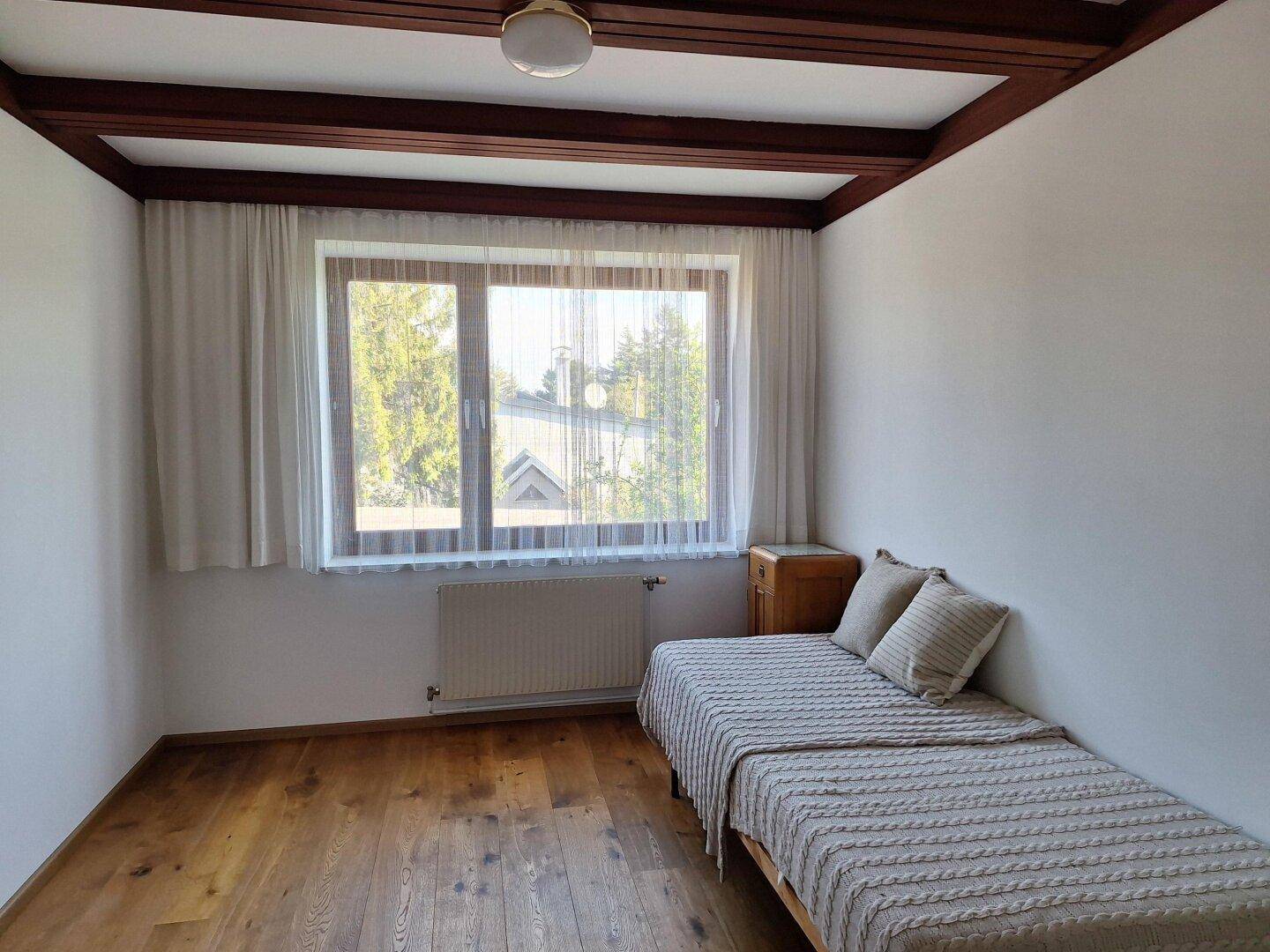Helles Schlafzimmer mit Holzboden, Fenster und einem Einzelbett.