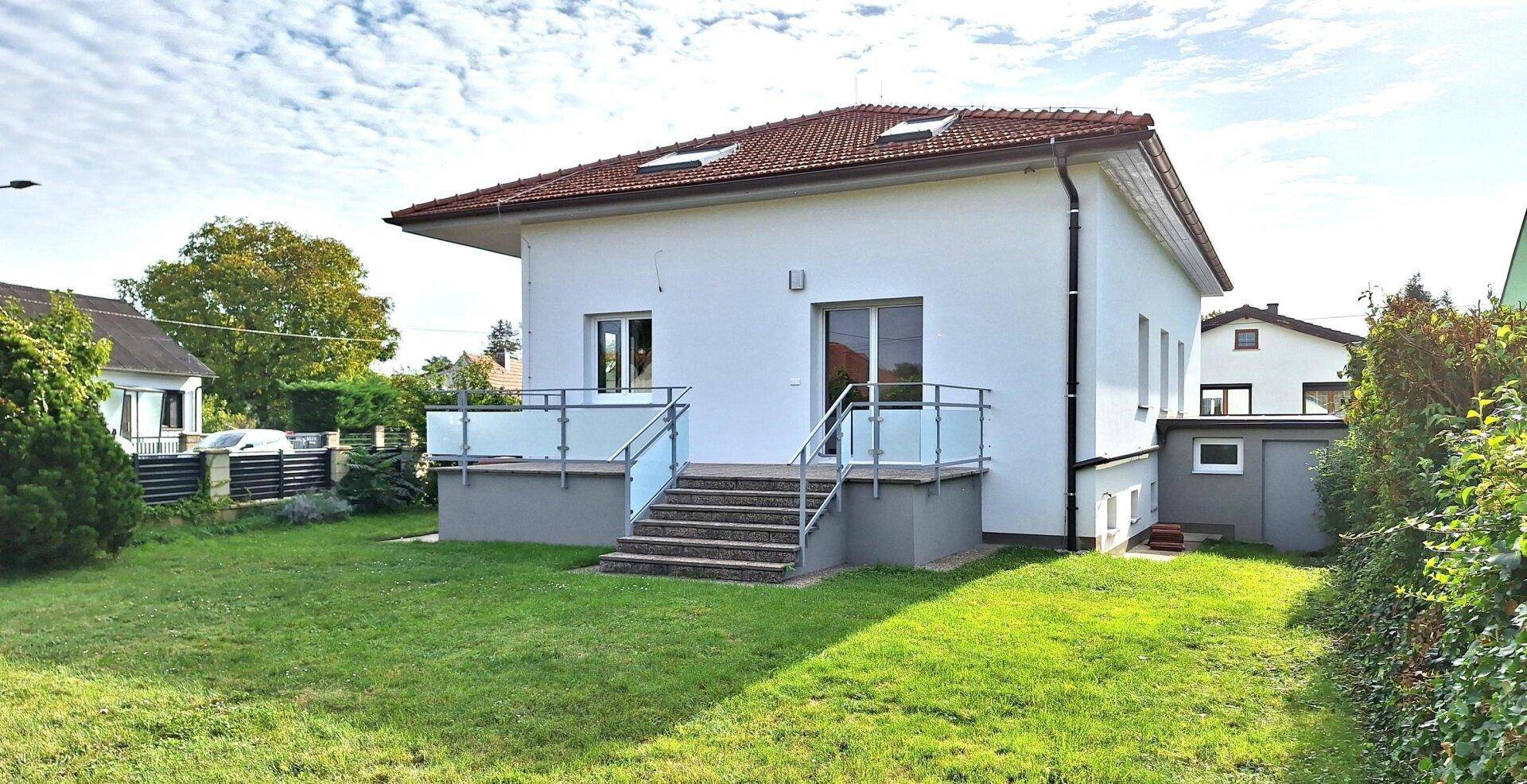 Rückansicht des Hauses mit Terrasse, Treppe zum Garten und gepflegter Rasenfläche.