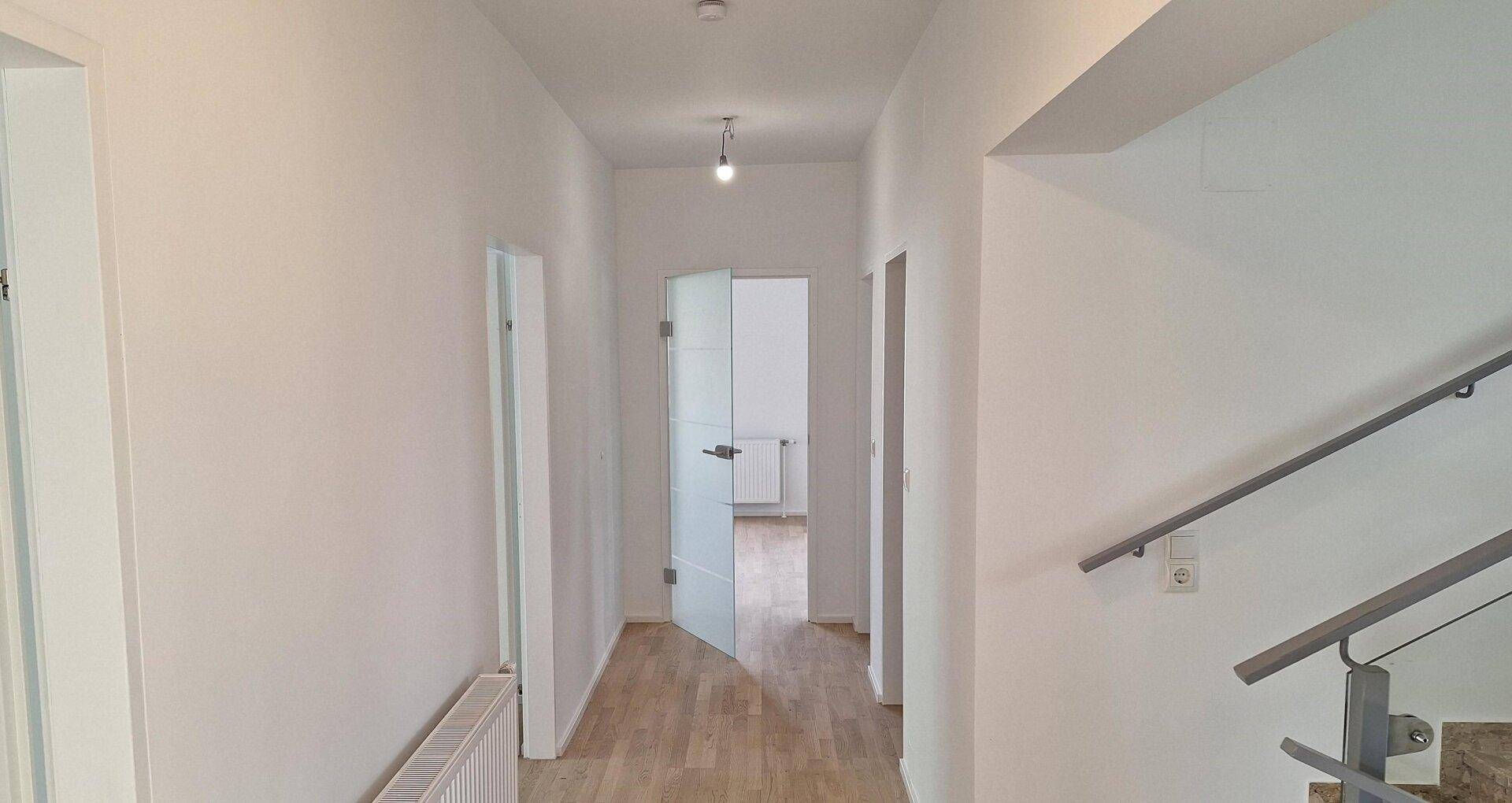 Langer, heller Flur mit Holzparkettboden und Zugang zu verschiedenen Zimmern im Erdgeschoss.