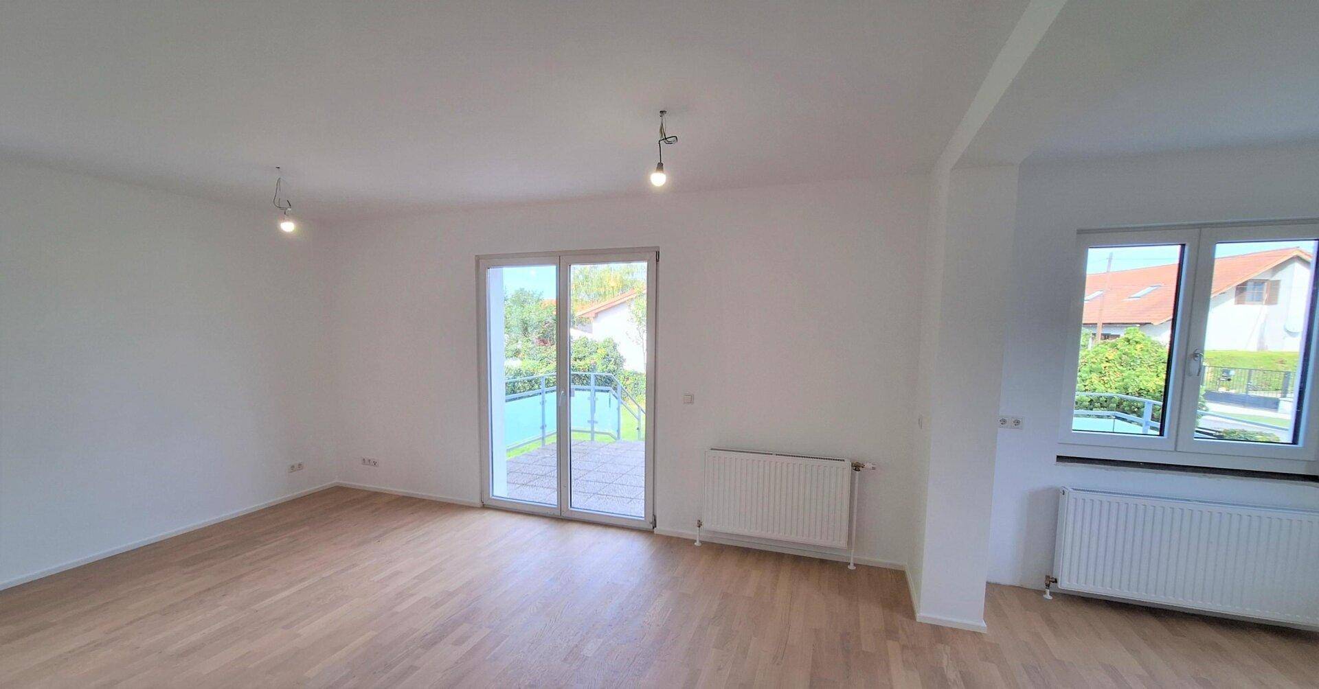 Helles Wohnzimmer mit Parkettboden, großen Fenstern und Zugang zur Terrasse.