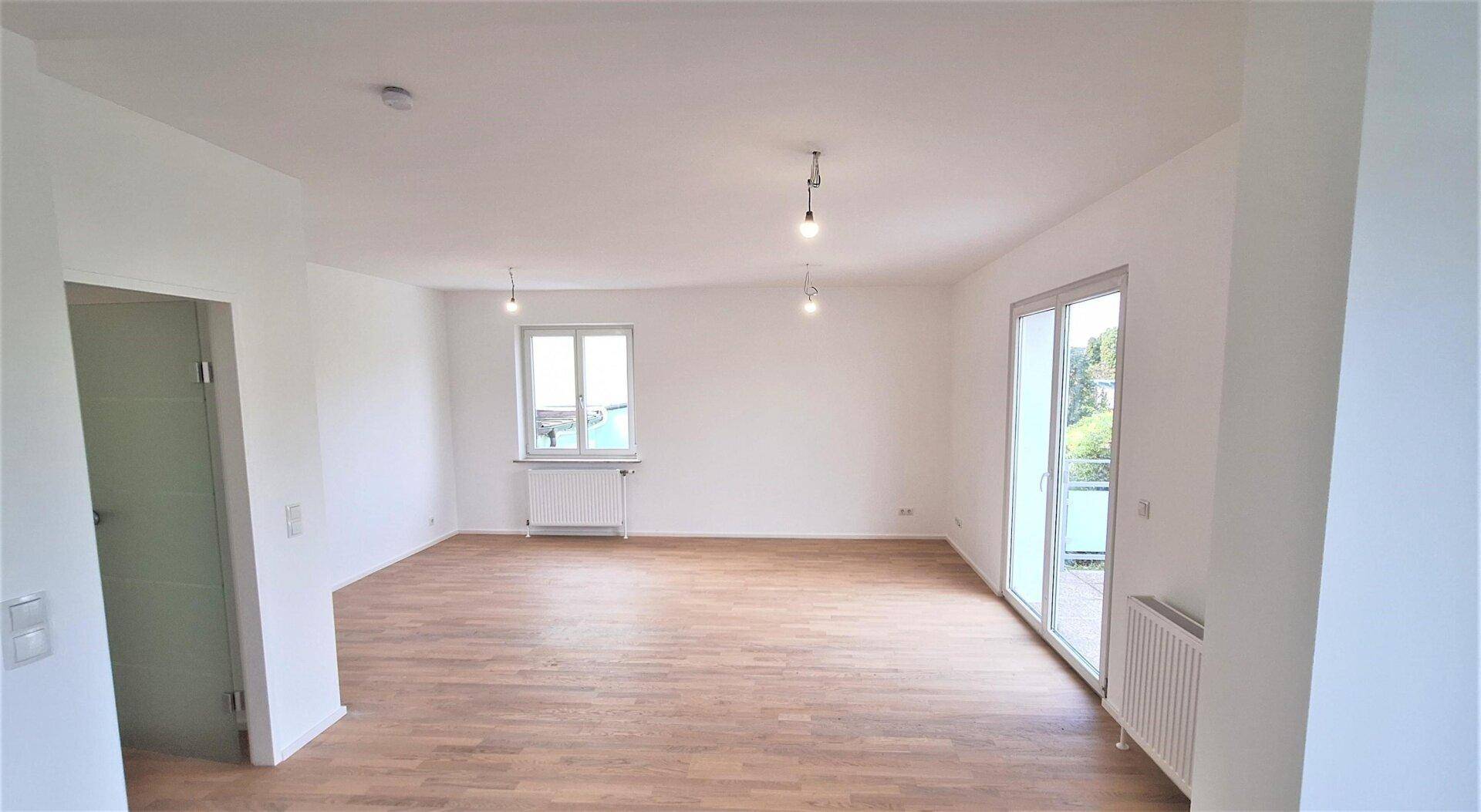 Weitläufiges Wohnzimmer mit hellem Parkettboden und viel Tageslicht durch große Fenster.