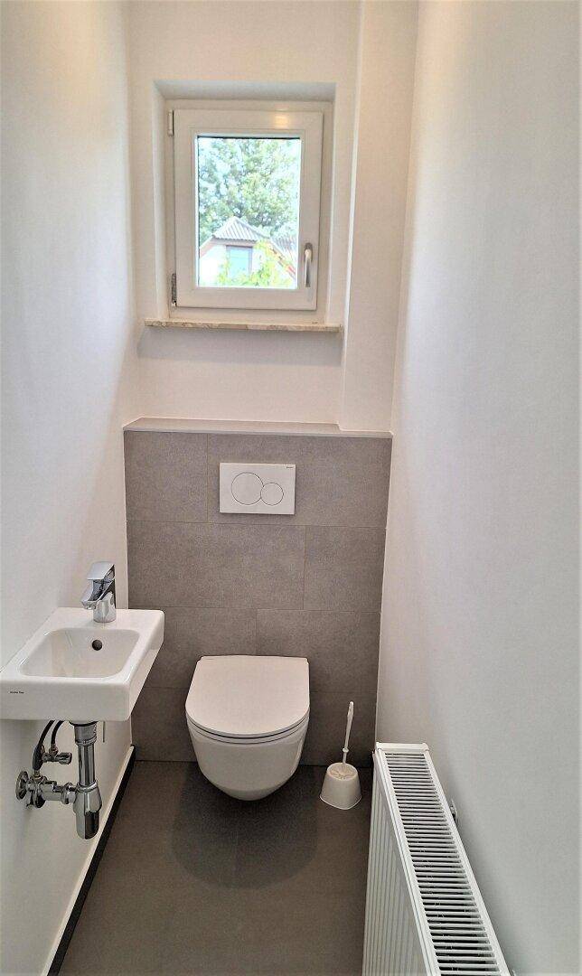 Kleines Gäste-WC mit wandhängender Toilette, Waschbecken und Fenster für Belüftung.