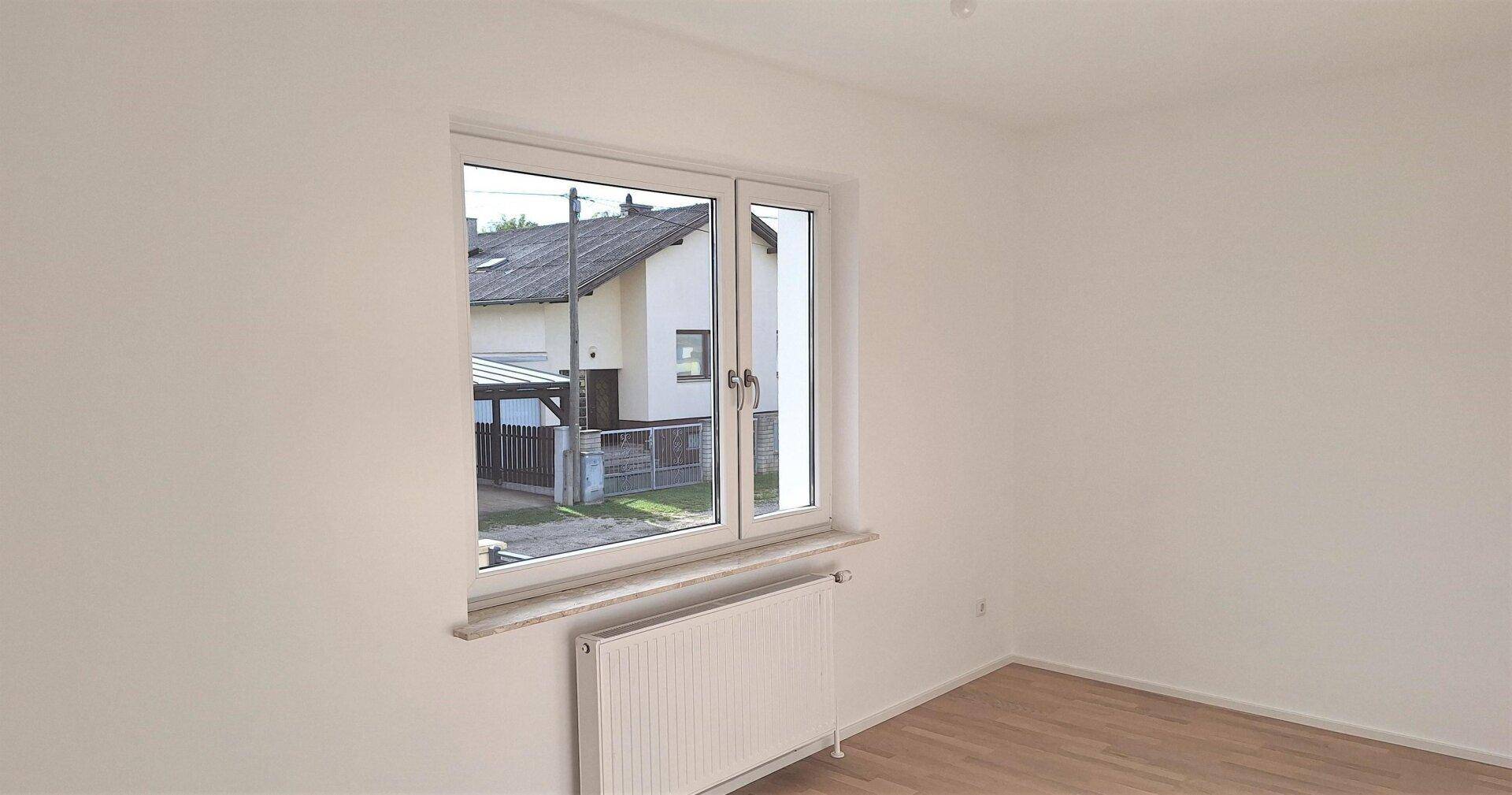 Ruhiges Zimmer mit Parkettboden und einem Fenster, das den Blick auf die Nachbarschaft freigibt.