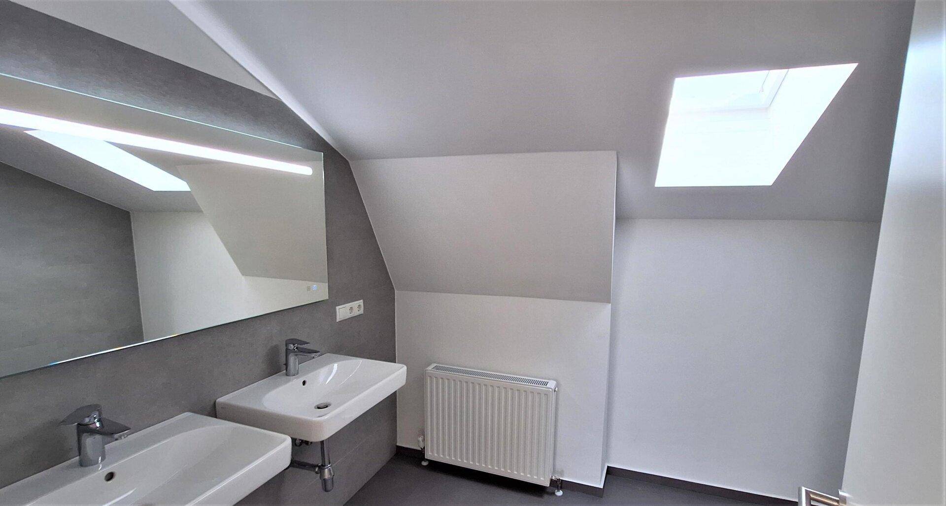 Modernes Badezimmer im Dachgeschoss mit Doppelwaschbecken, Dachfenster und schrägen Wänden.