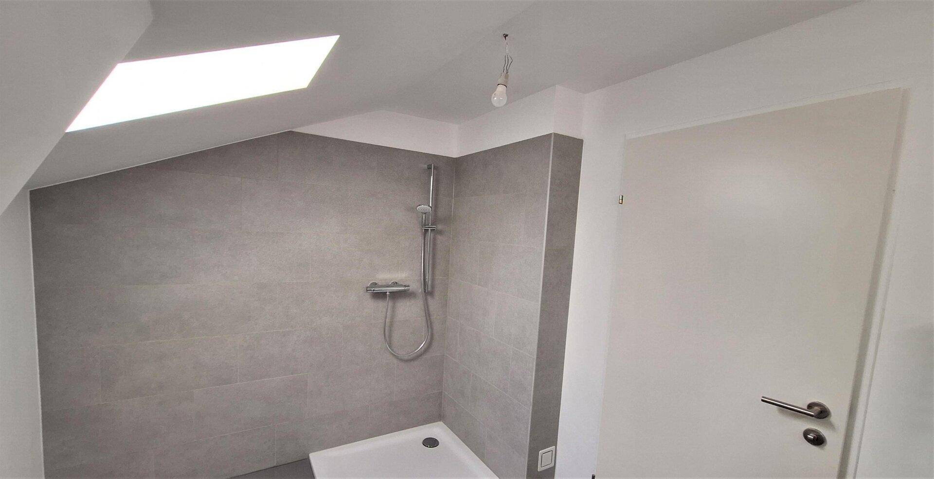 Duschbereich im modernen Badezimmer im Dachgeschoss mit grauen Fliesen und Dachfenster.