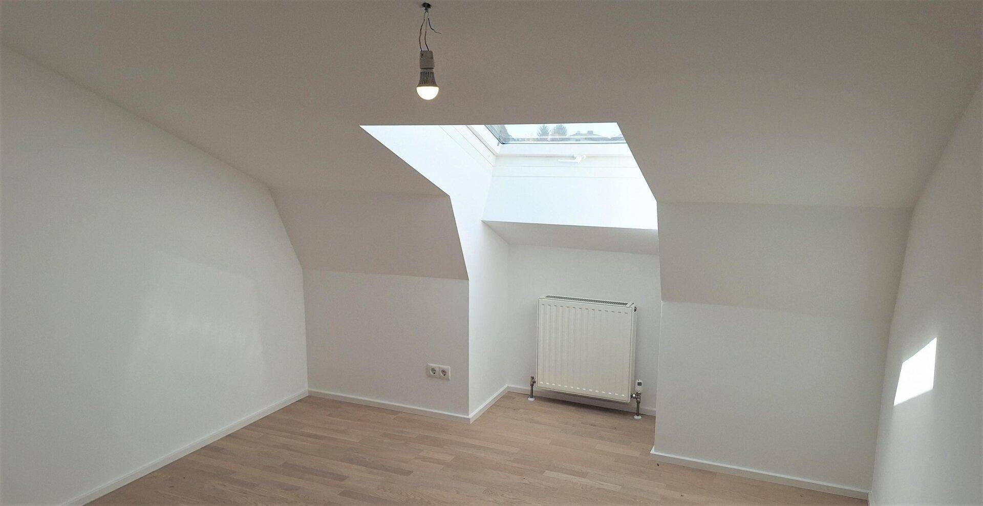 Heller Raum im Dachgeschoss mit Schrägdach, Dachfenster und neuem Laminatboden.