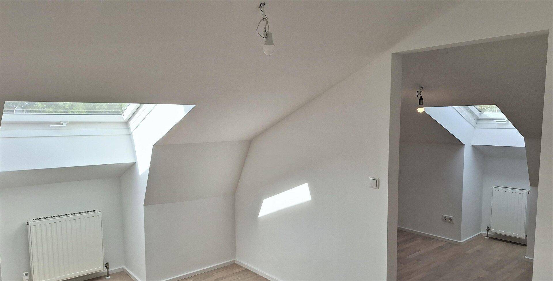 Dachgeschossraum mit zwei Dachfenstern, Schrägdach und hellem Laminatboden, bereit zum Einzug.
