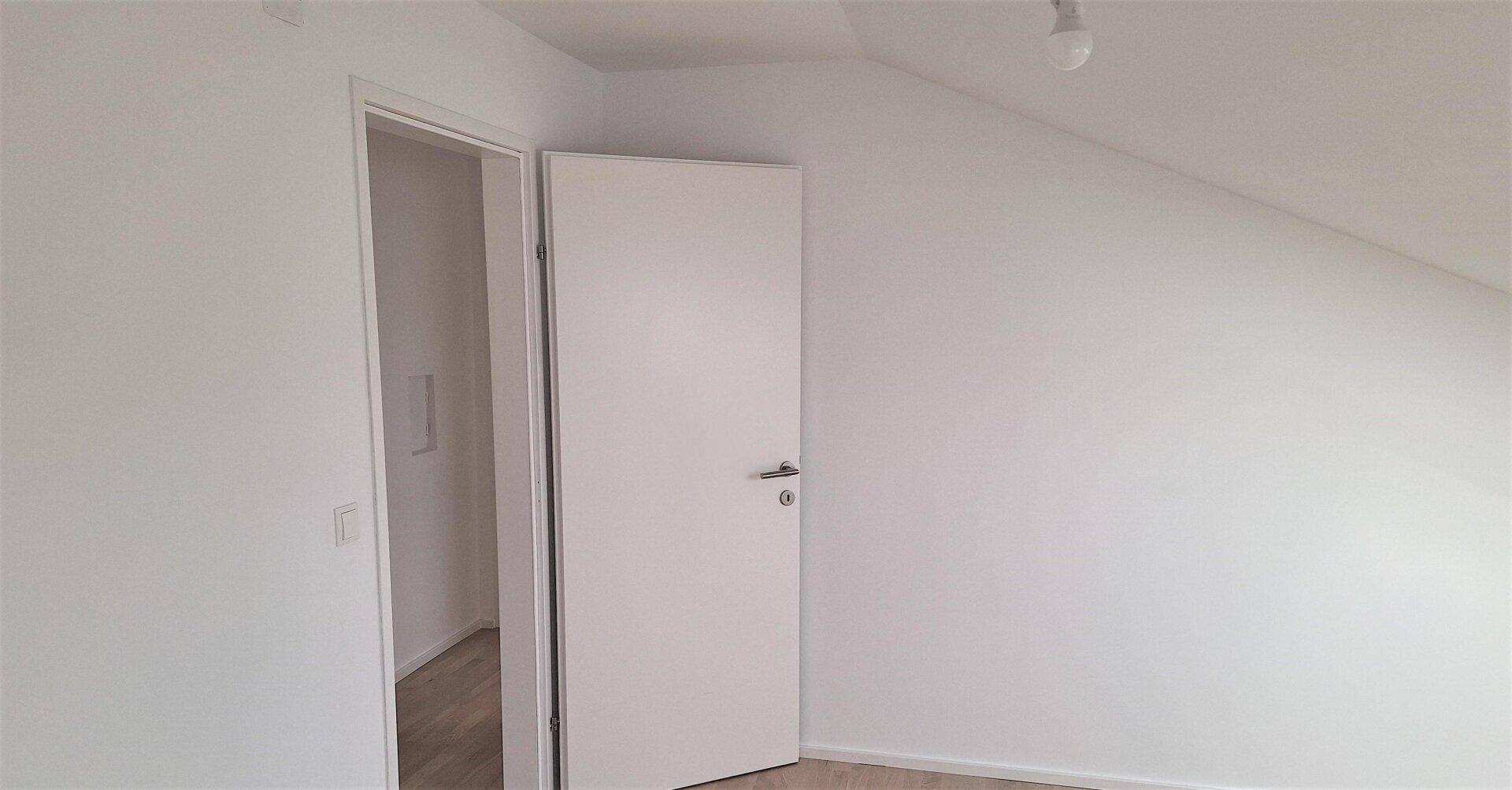 Weiße Tür in einem hellen Raum mit Schrägdach und sauberem Laminatboden, frisch gestrichen.
