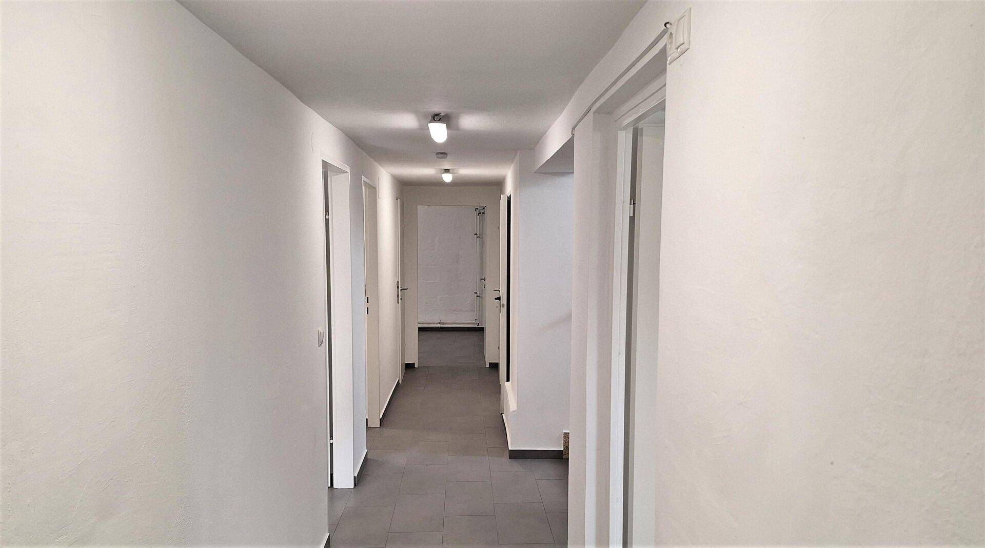 Langer, heller Flur mit grauem Fliesenboden und mehreren Türen, gut beleuchtet.