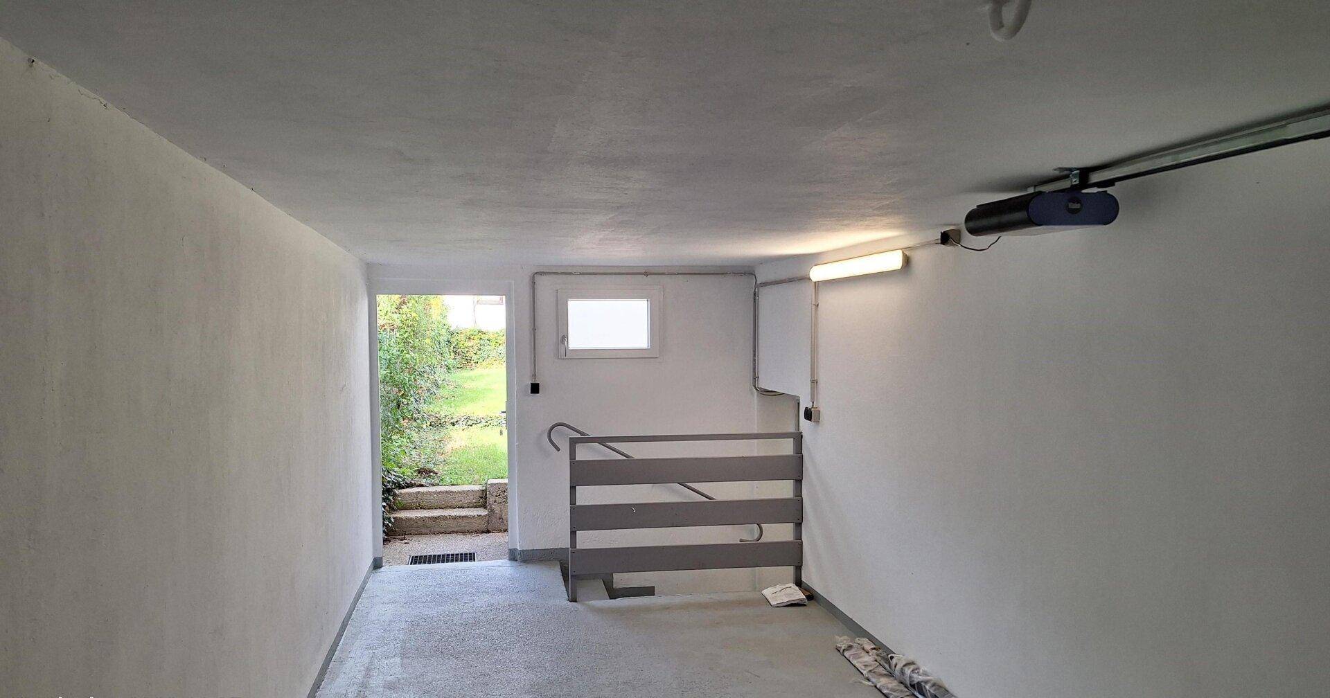 Helle Garage mit direktem Zugang zum Garten und Betonboden, ideal für Fahrzeuge.
