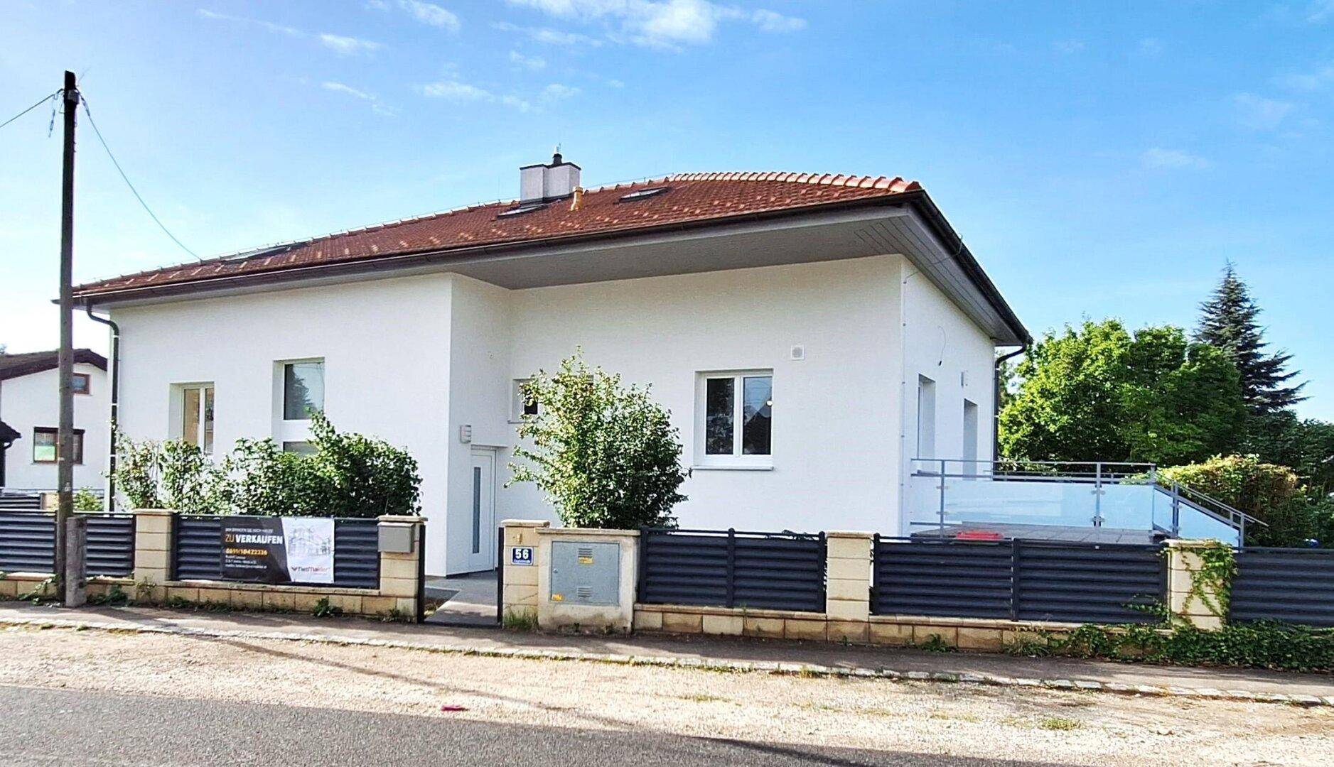 Modernes Einfamilienhaus mit weißer Fassade, rotem Ziegeldach und gepflegtem Vorgarten.
