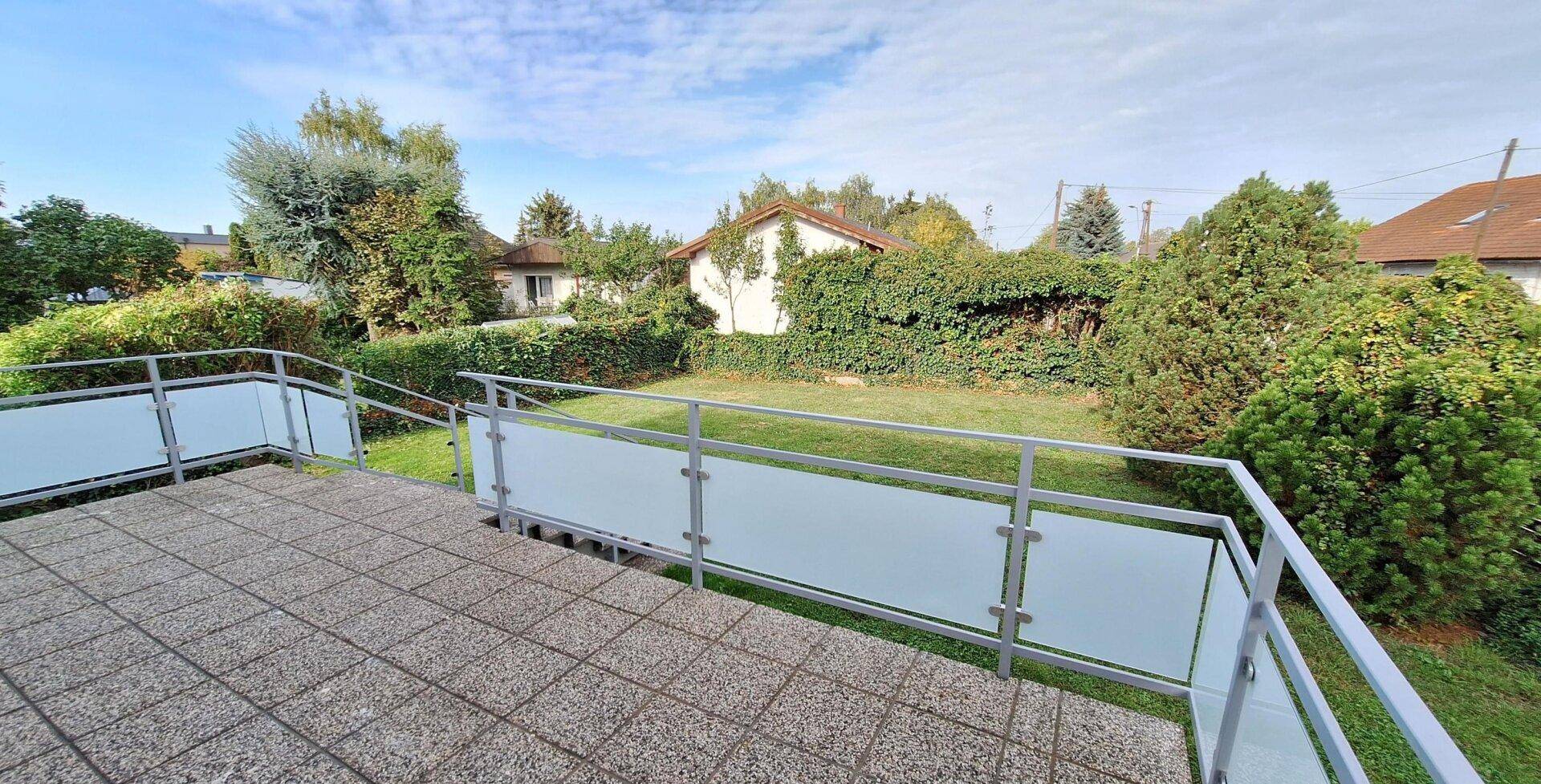Große Terrasse mit Fliesenboden und Glasbrüstung, bietet einen schönen Blick in den Garten.