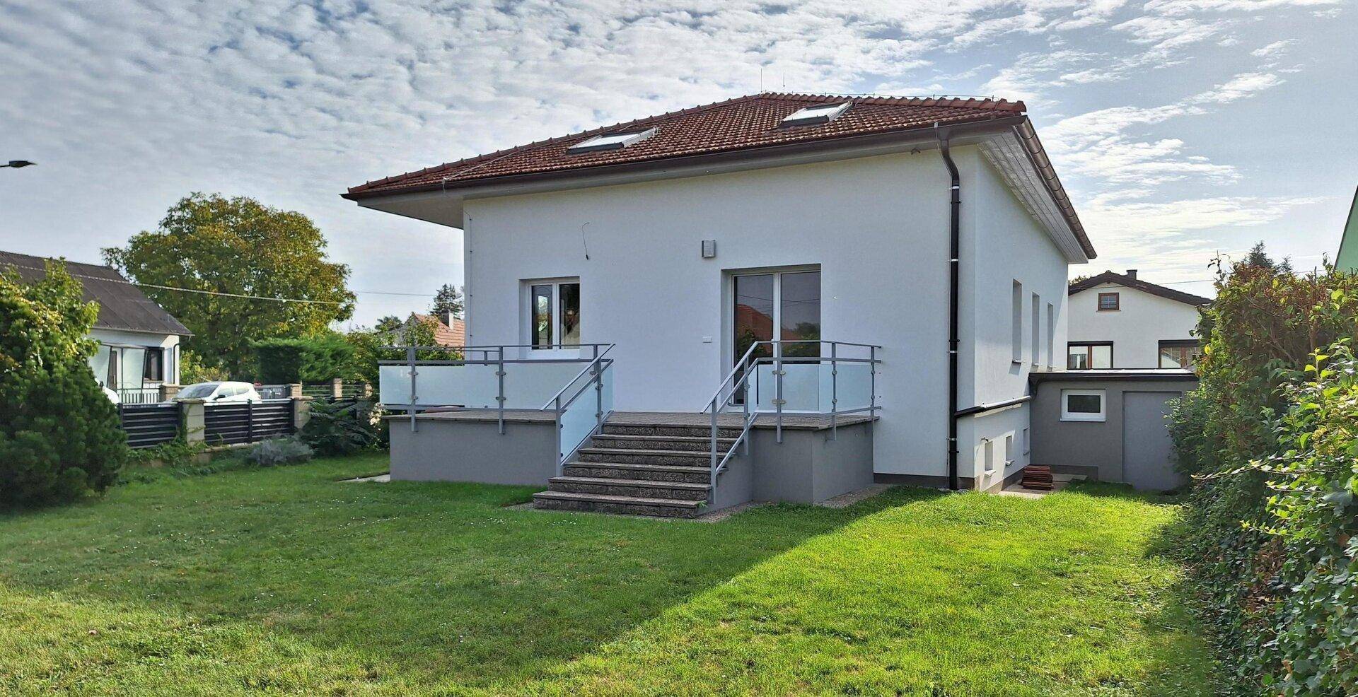 Rückseite des Hauses mit Terrasse, Treppe zum Garten und grüner Rasenfläche.