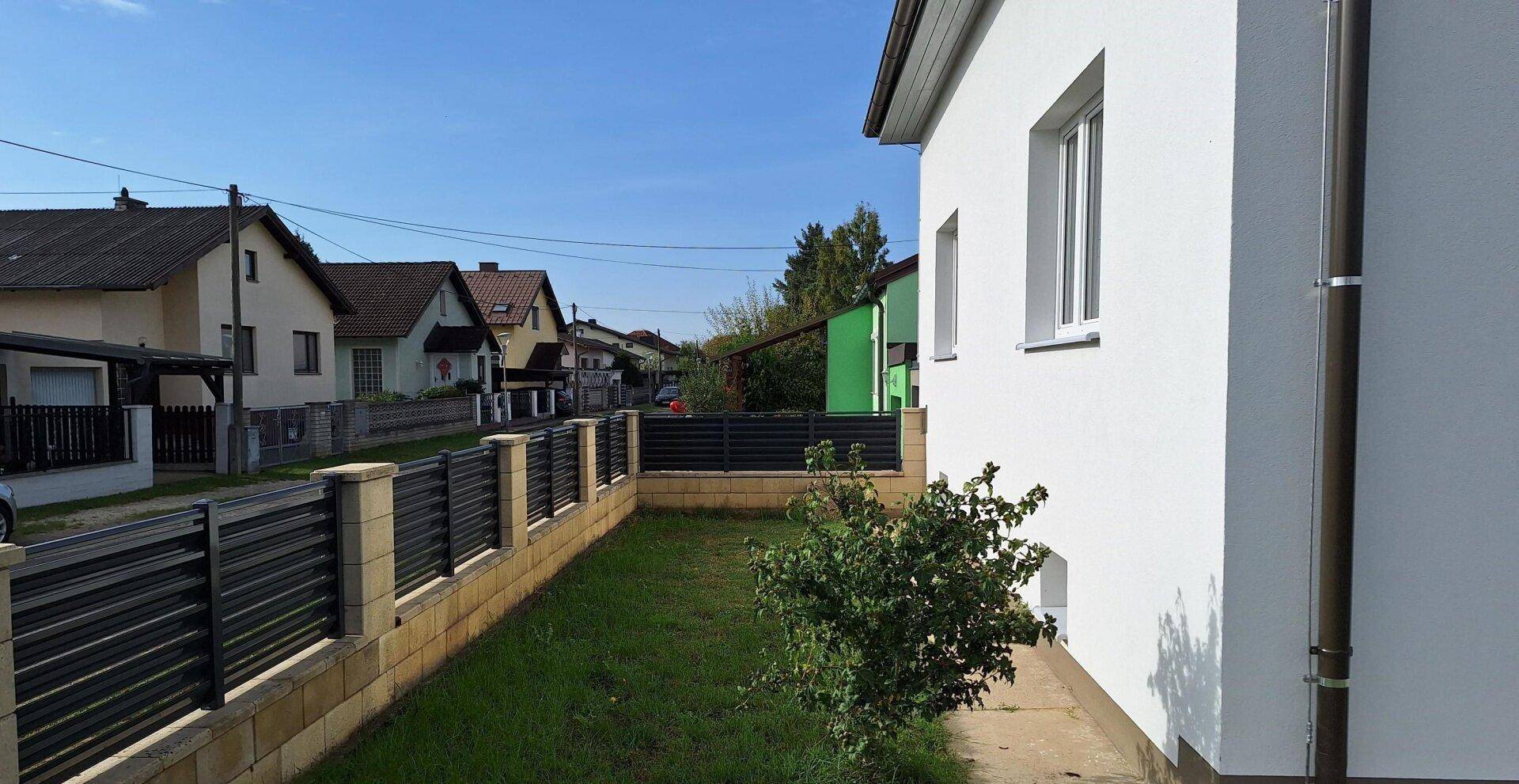 Seitenansicht des Hauses mit Zaun und Blick auf die ruhige Wohnstraße.