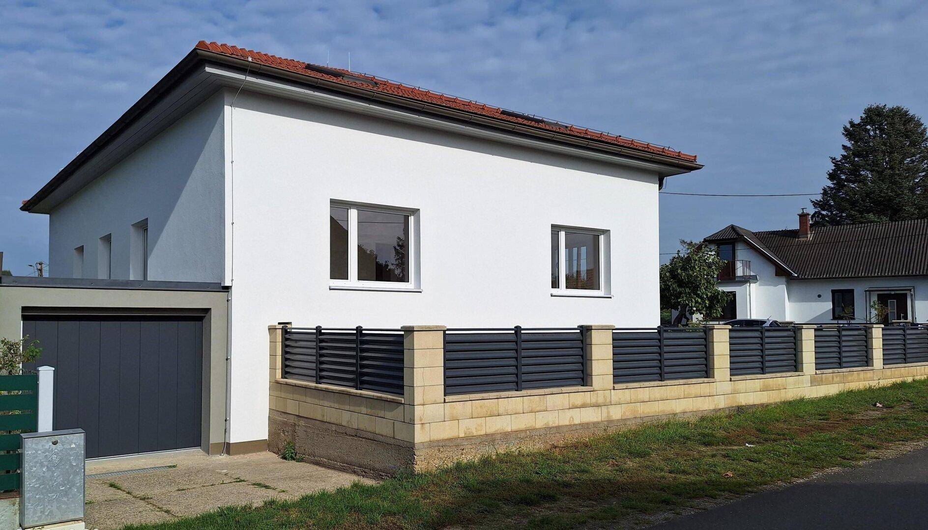 Seitenansicht des Hauses mit Garage, Zaun und rotem Ziegeldach, gut gepflegt.