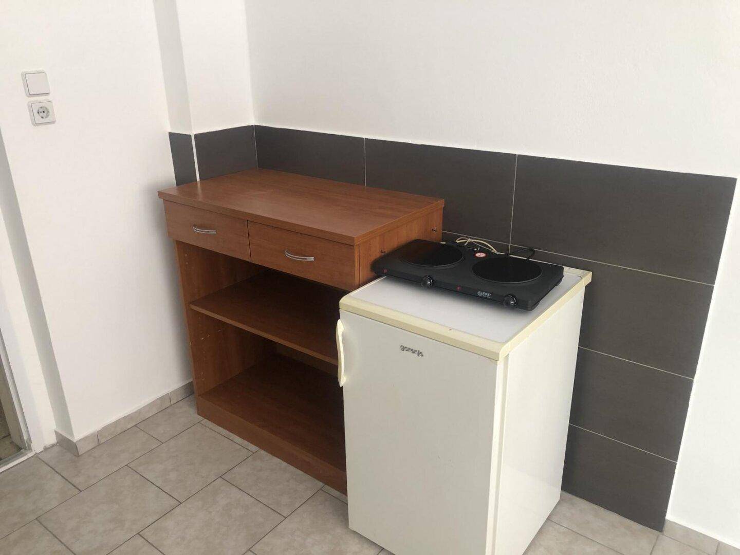 Kleine Kochnische mit Kühlschrank, mobiler Kochplatte und Ablagefläche.