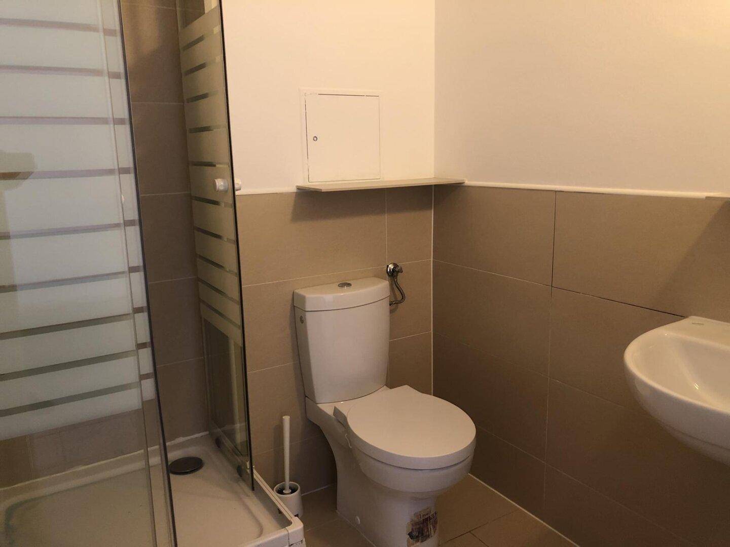 Funktionales Badezimmer mit Duschkabine, Toilette und Waschbecken, gefliest in Beige und Weiß.