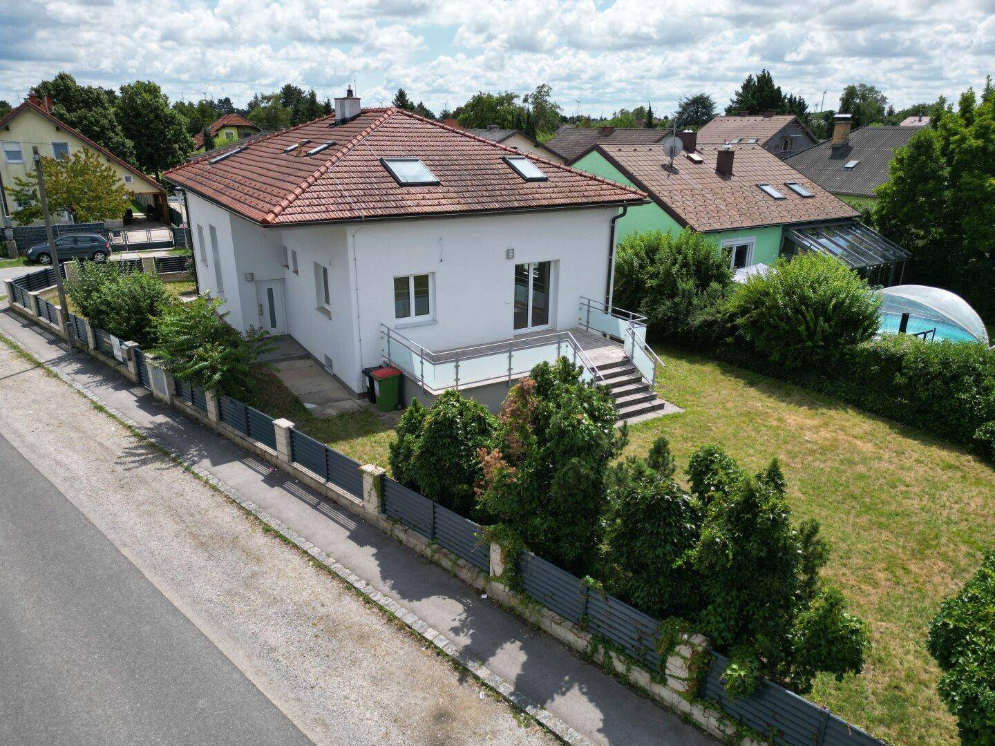 Luftaufnahme des Einfamilienhauses mit Garten, Terrasse und kleinem Pool unter bewölktem Himmel.